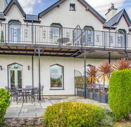An exterior view of a two-story house with a balcony and patio furniture on a paved area at Menai View in Llanfairpwllgwyngyll near Beaumaris