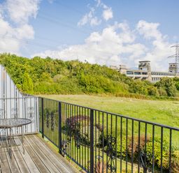 A balcony with a metal table and two chairs overlooking a grassy field and trees at Menai View in Llanfairpwllgwyngyll near Beaumaris