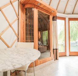 A marble table with a chair next to a wooden sauna and glass doors at Island Yurt in Beckford near Tewkesbury