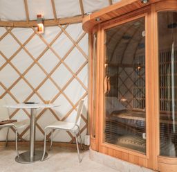 A small seating area with two chairs and a round table next to a wooden sauna at Island Yurt Beckford near Tewkesbury