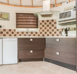 A kitchen with brown cabinets white appliances a microwave and a window with a brown blind at Island Yurt Beckford near Tewkesbury