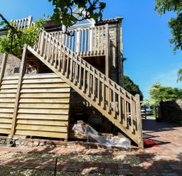 An exterior view of a stone building with wooden stairs leading to an upper door at The Loft at Lucott House in Bath