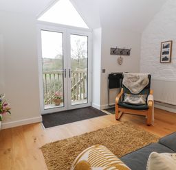 A living room with glass doors leading outside a wooden deck a chair with a cushion and throw and a TV mounted on the wall at The Loft at Lucott House in Bath