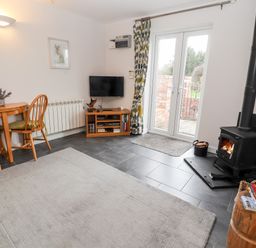 A living room with a wood burning stove table with chairs and a television at The Old Stable in Mold