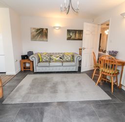 A living room with a grey sofa and cushions a wooden dining table with chairs and a rug on the floor at The Old Stable in Mold