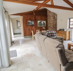 A living room with a beige sofa a wooden dining table wooden furniture exposed ceiling beams and a brick chimney at The Old Dairy in Newnham-on-Severn