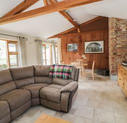 A living room with a sectional sofa wooden dining table and chairs wooden sideboard and exposed brick wall at The Old Dairy in Newnham-on-Severn
