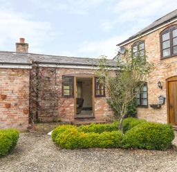 A brick exterior house with wooden door and windows surrounded by shrubs and gravel at The Old Dairy in Newnham-on-Severn