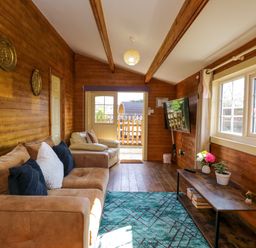 A living room with wooden walls a brown sofa an armchair a wall-mounted TV and a table with flowers at The Nook in Royal Wootton Bassett