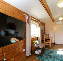 A living room with a mounted television flowers on a coffee table and a small dining table at The Nook in Royal Wootton Bassett