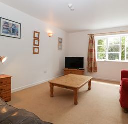 A living room with a wooden coffee table a red armchair a black sofa a wooden side table with a lamp and a TV on a wooden stand under a window at Wheelbarrow Cottage in Stoke Prior near Leominster