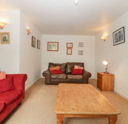A living room with a red sofa brown leather sofa wooden coffee table and side table with lamp at Wheelbarrow Cottage in Stoke Prior near Leominster
