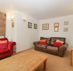A living room with a red sofa a brown leather sofa a wooden coffee table and framed pictures on the wall at Wheelbarrow Cottage in Stoke Prior near Leominster