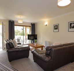 A living room with two brown leather sofas a wooden coffee table a television and sliding glass doors at Stone Water Cottage in Strathpeffer