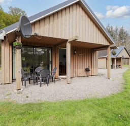 A wooden cabin with outdoor chairs and table on gravel near grass at Pebbles Cottage in Achilty near Strathpeffer