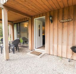 A covered outdoor area with a small table and four chairs a barbecue grill and an open door at Pebbles Cottage in Achilty near Strathpeffer