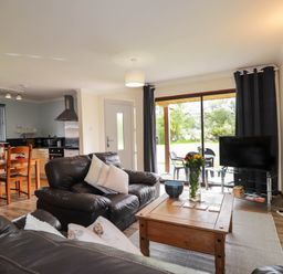 A living room with black leather sofas a wooden coffee table a television and dining table at Pebbles Cottage in Achilty near Strathpeffer