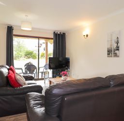 A living room with leather sofas a coffee table a television and a sliding glass door leading to an outdoor seating area at Pebbles Cottage in Achilty near Strathpeffer