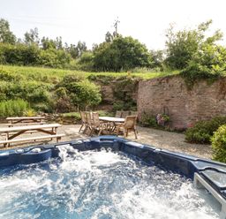 An outdoor seating area with wooden picnic tables and chairs with a hot tub in the foreground at Wheelbarrow Castle in Leominster