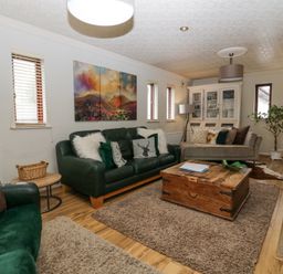 A living room with green and beige sofas a wooden coffee table a white cabinet and a plant at Sandown in Bowness-on-Windermere