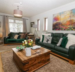 A living room with green sofas and a wooden coffee table with flowers at Sandown in Bowness-on-Windermere