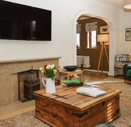 A living room with a wooden coffee table flowers on it a mounted TV and an arched doorway at Sandown in Bowness-on-Windermere