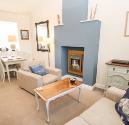 A living room with armchairs a coffee table a fireplace and a dining table in the corner at Driftwood Apartment in Amble-by-the-Sea