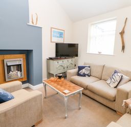 A living room with two beige sofas a wooden coffee table a fireplace a television on a cabinet and windows at Driftwood Apartment in Amble-by-the-Sea