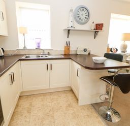 A kitchen with white cabinets a double sink a dark countertop a bar stool and a dining area with chairs at Driftwood Apartment in Amble-by-the-Sea