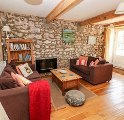 A living room with two brown sofas a wooden coffee table a bookshelf and a stone wall at Beekeeper's Cottage in Pembroke