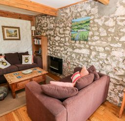 A living room with two brown sofas a wooden coffee table and stone walls at Beekeeper's Cottage in Pembroke