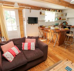 A living room with a sofa and cushions next to a kitchen with a wooden island and bar stools at Beekeeper's Cottage in Pembroke