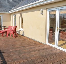 A wooden deck with red patio furniture and glass doors at Bluebell House and Gardens in Gurteenulla near Ballydehob County Cork