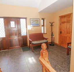 A hallway with a wooden front door a wooden bench a coat rack an umbrella and a fire extinguisher at Bluebell House and Gardens Gurteenulla near Ballydehob County Cork