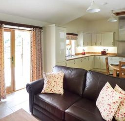 A kitchen and living area with a dark sofa and floral cushions near wooden dining chairs and a glass door at Beudy in Llangwm near Bala