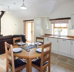 A kitchen and dining area with a round wooden table set for four and a sofa in the background at Beudy in Llangwm near Bala