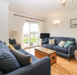 A living room with two blue sofas a wooden chest as a coffee table and a tv near a sliding glass door at Broom Cottage Stoneleigh Holiday Village near Sidmouth