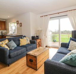 A living room with two blue sofas and wooden chest table near sliding glass doors at Broom Cottage in Stoneleigh Holiday Village near Sidmouth