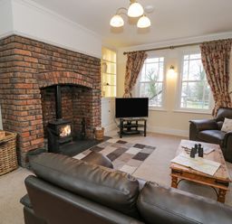 A living room with a brick fireplace leather sofas a wooden coffee table and a television at The Farm House in Bala