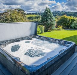 An outdoor hot tub with bubbling water in a garden with trees and hills in the background at The Farm House in Bala