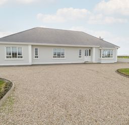 A single story house with multiple windows and a large gravel driveway at Shraigh Beach in Belmullet County Mayo