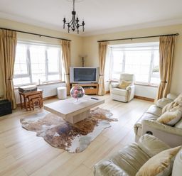 A living room with cream sofas a coffee table a TV and large windows at Shraigh Beach in Belmullet County Mayo