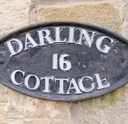 A metal oval sign with the text Darling 16 Cottage on a stone wall at Darling Cottage in Bamburgh