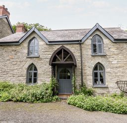 A stone cottage with arched windows and a blue wooden door surrounded by plants at Maesgwyn in Bridell near Cardigan
