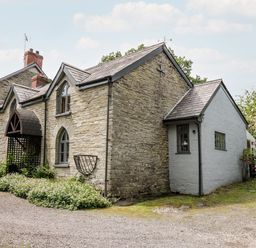 A stone house with arched windows and a wooden porch surrounded by plants at Maesgwyn Bridell near Cardigan