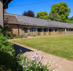 A long single story building with a slate roof and garden with flowers and picnic table at Keepers Cottage in Winterborne Stickland