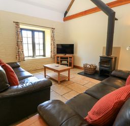 A living room with two black leather sofas red cushions a wood burning stove and a television at Keepers Cottage in Winterborne Stickland