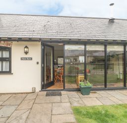 An exterior view of a building with a tiled roof a glass door and windows a plant in a pot on the patio at New Barn in Winterborne Stickland
