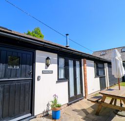 Exterior view of a building with black doors and windows a wooden picnic table and umbrella on a patio at Rowdens Barn in Winterborne Stickland