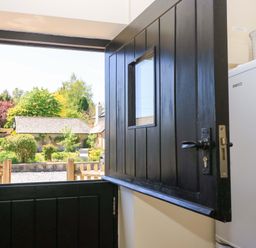 An open stable door with a window showing a garden and wooden fence at Rowdens Barn in Winterborne Stickland